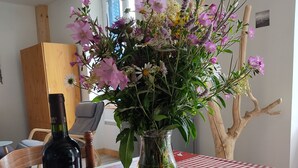 Un tavolo con tovaglia a quadri, una bottiglia di vino, un vaso con fiori e una sedia.