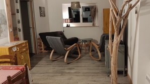 Un soggiorno accogliente con pavimento in legno, una poltrona a dondolo, un tavolino e una finestra con una lampada.