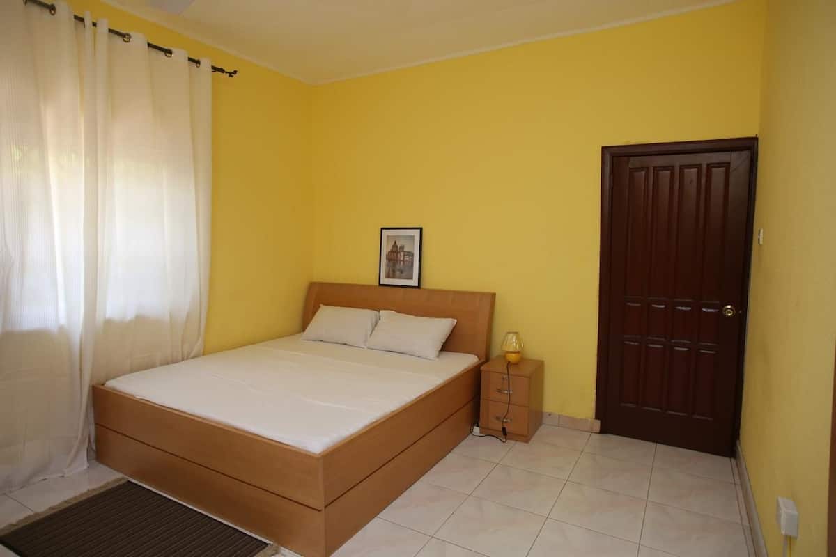 Un dormitorio con cama de madera, una mesita de noche, una puerta y un cuadro en la pared.