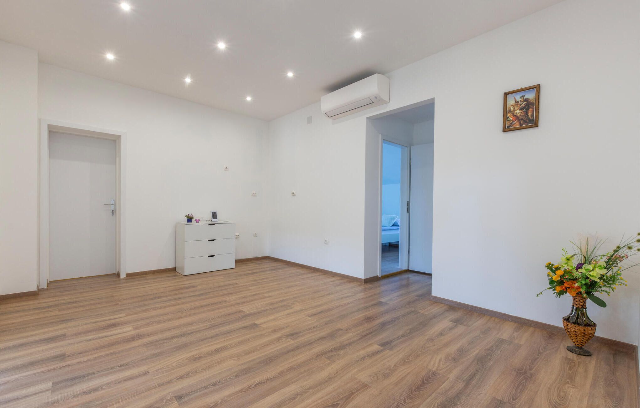 A spacious room with wooden flooring, a white dresser, an air conditioning unit, and a door leading to another room.