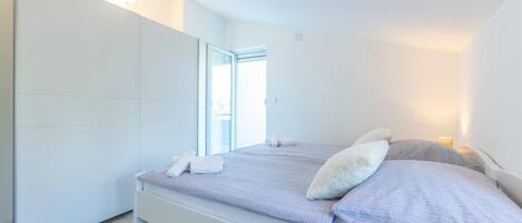 A modern bedroom with a bed, a wardrobe, and a window.