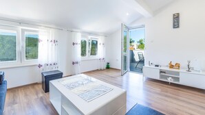 Een moderne, goed verlichte kamer met grote ramen, een witte tafel in het midden en een glazen deur naar een buitenruimte.