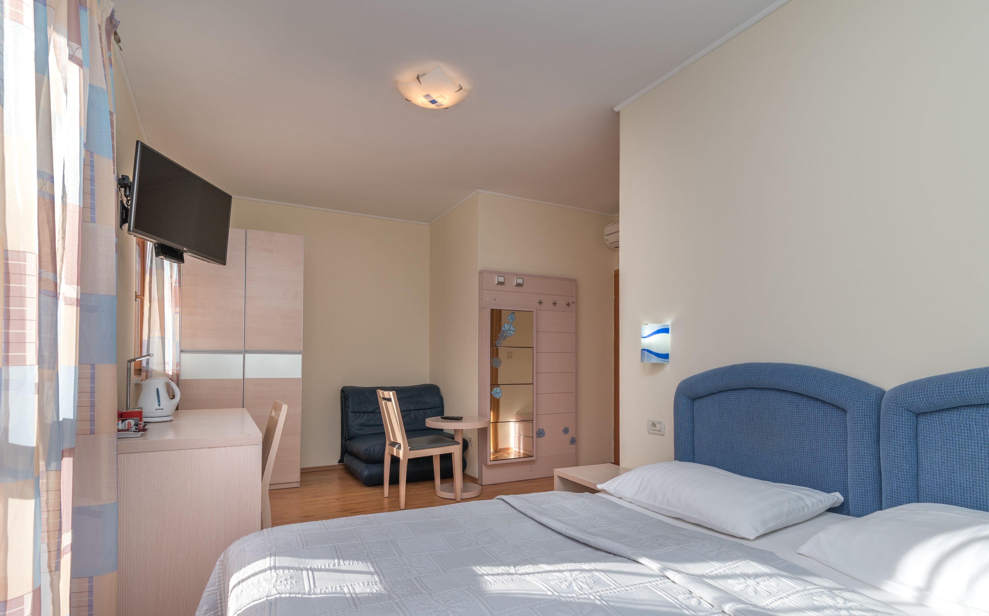 Ein Hotelzimmer mit Bett, Schreibtisch, Stuhl, Kleiderschrank und Fernseher.