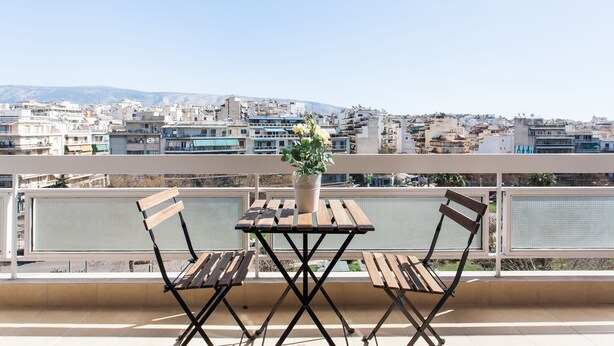 Ein Balkon mit Holztisch und Stühlen, einem Topfpflanzen und einer Blick auf die Stadt im Hintergrund.