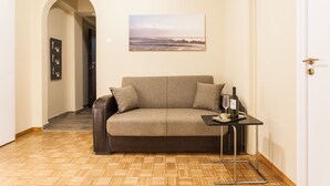 Ein gemütliches Zimmer mit einer Couch, einem kleinen Tisch mit Flasche und Glas sowie einem Bild an der Wand.