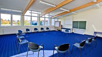 Un salón de conferencias con alfombra azul, vigas de madera y ventanas amplias.