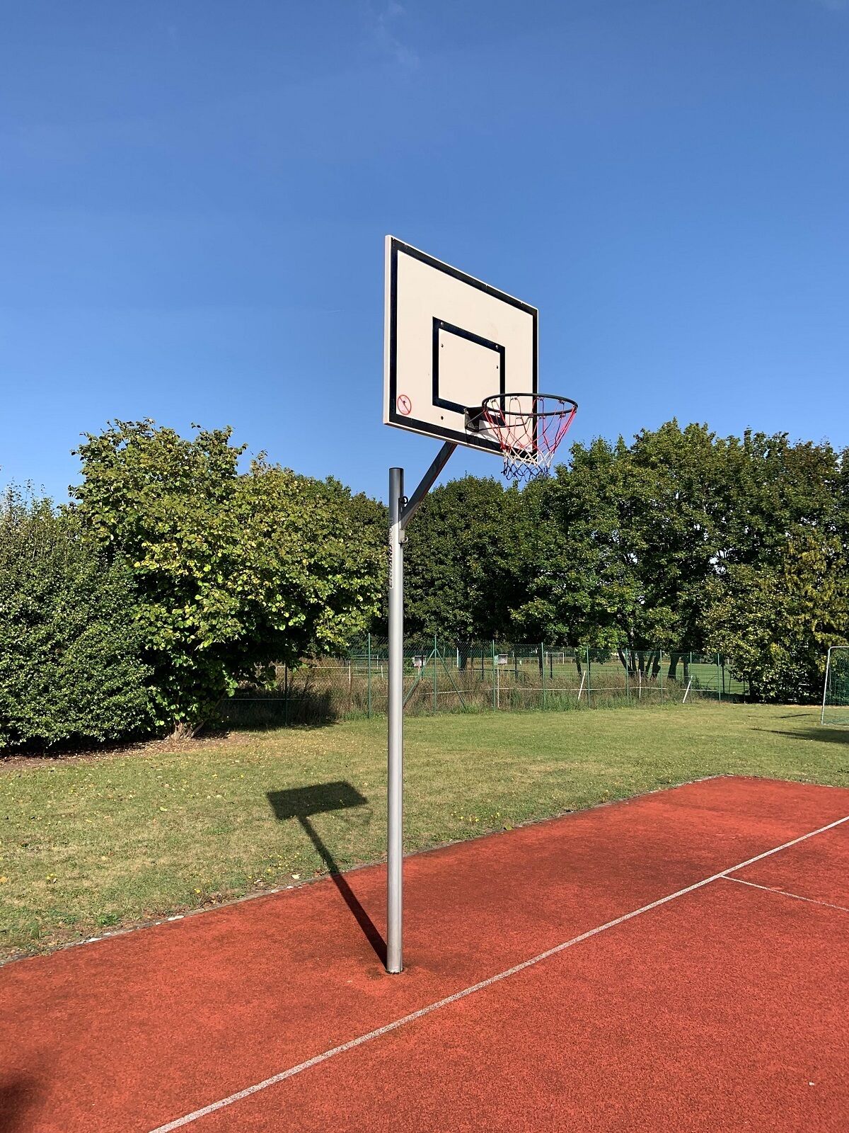 A basketball court with a hoop and a red surface.