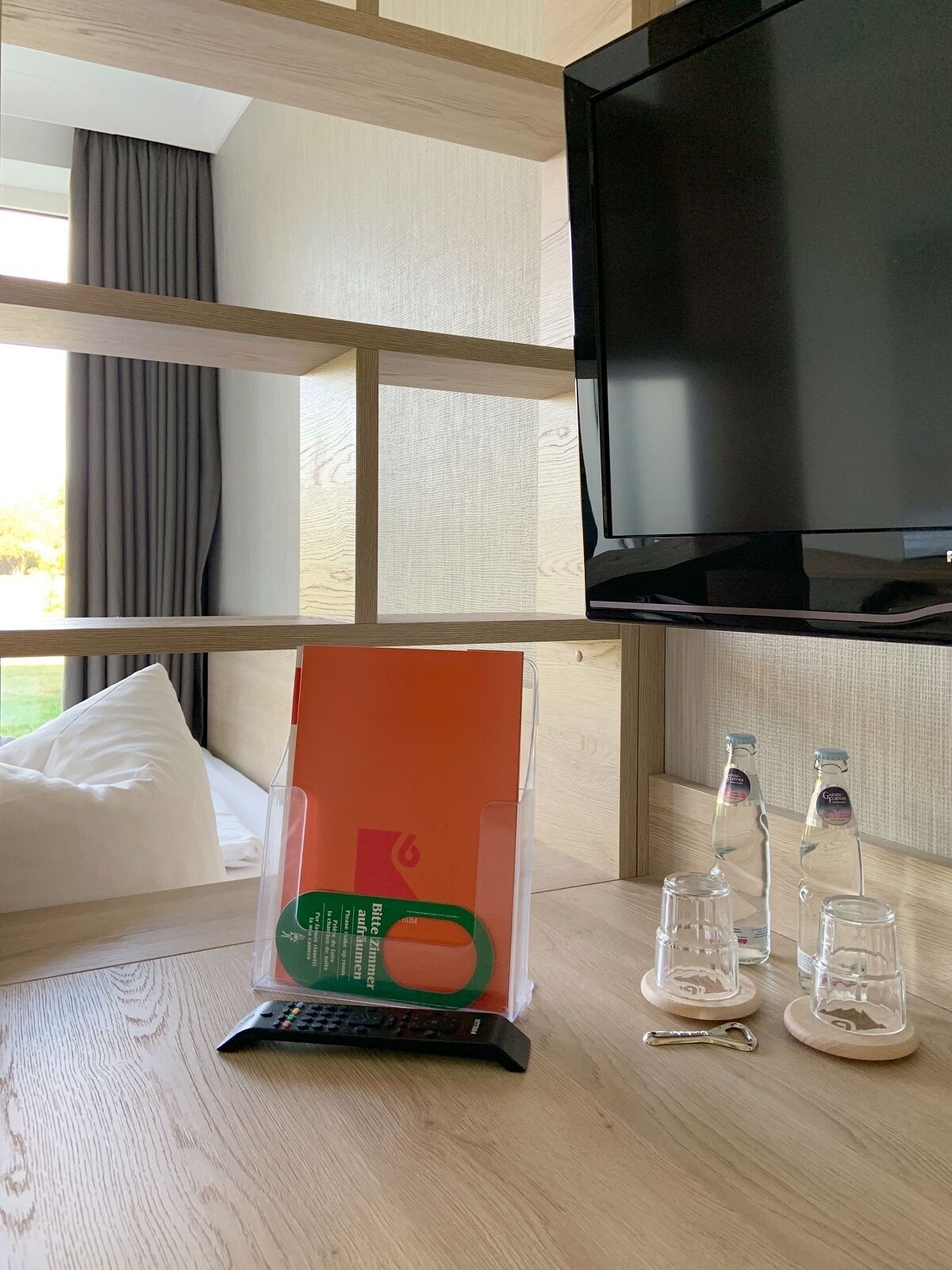Hotelkamer met een bed, een televisie, een tafeltje met een afstandsbediening, een fles en een glas.