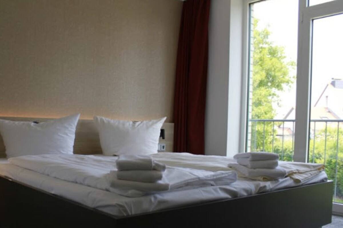 A hotel room with a bed, pillows, and a window with a view of greenery.