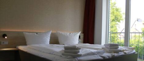 A hotel room with a bed, pillows, and a window with a view of greenery.