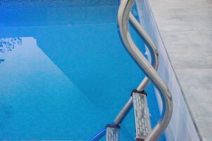 Una piscina con agua azul cristalina y una escalera de metal.