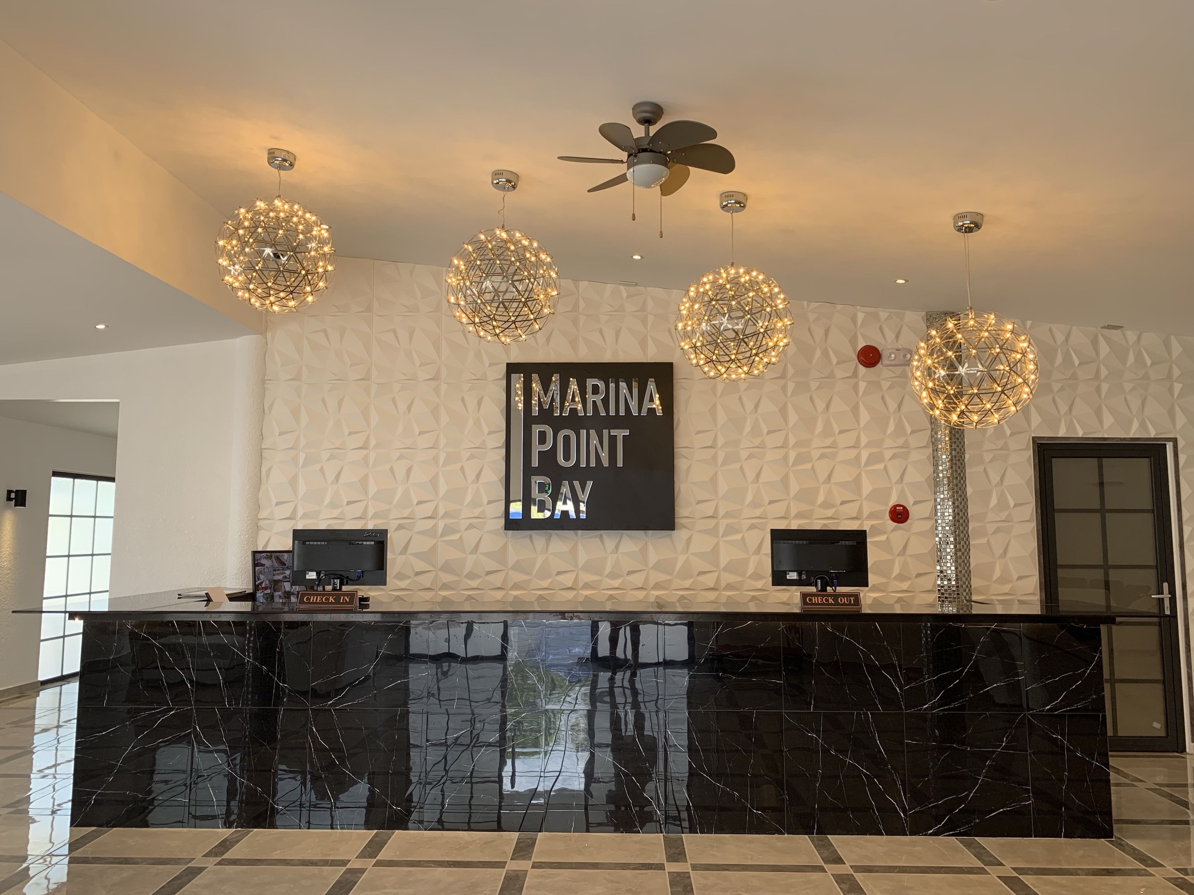 A reception desk with a black marble top, two monitors, and a sign that reads "MARINA POINT BAY".