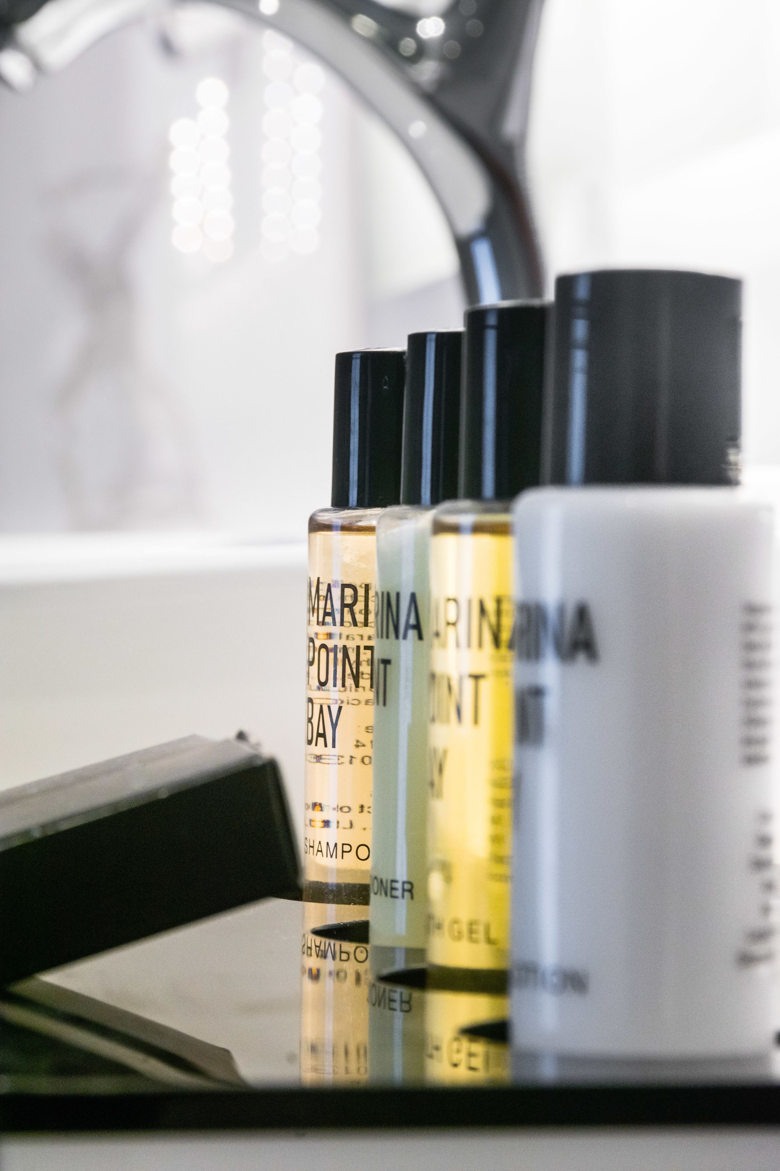 A row of toiletries on a table, including a bottle labeled "MARINA RINEMA POINT BAY SHAMPOO".