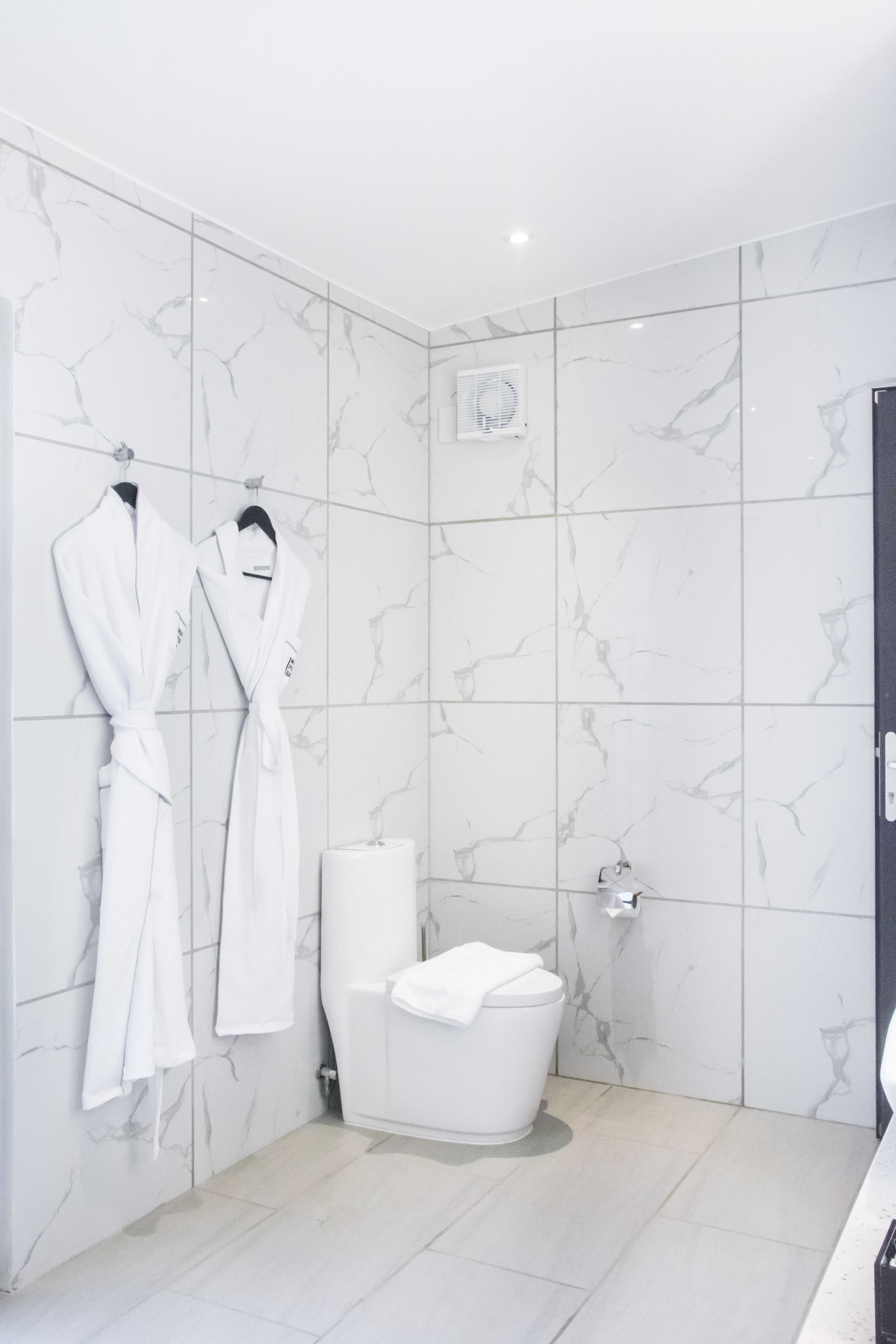 A modern bathroom with marble tiles, a white toilet, and two white bathrobes hanging on the wall.