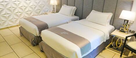 A hotel room with two beds, a small bedside table with a lamp, a chair, and a decorative wall panel.