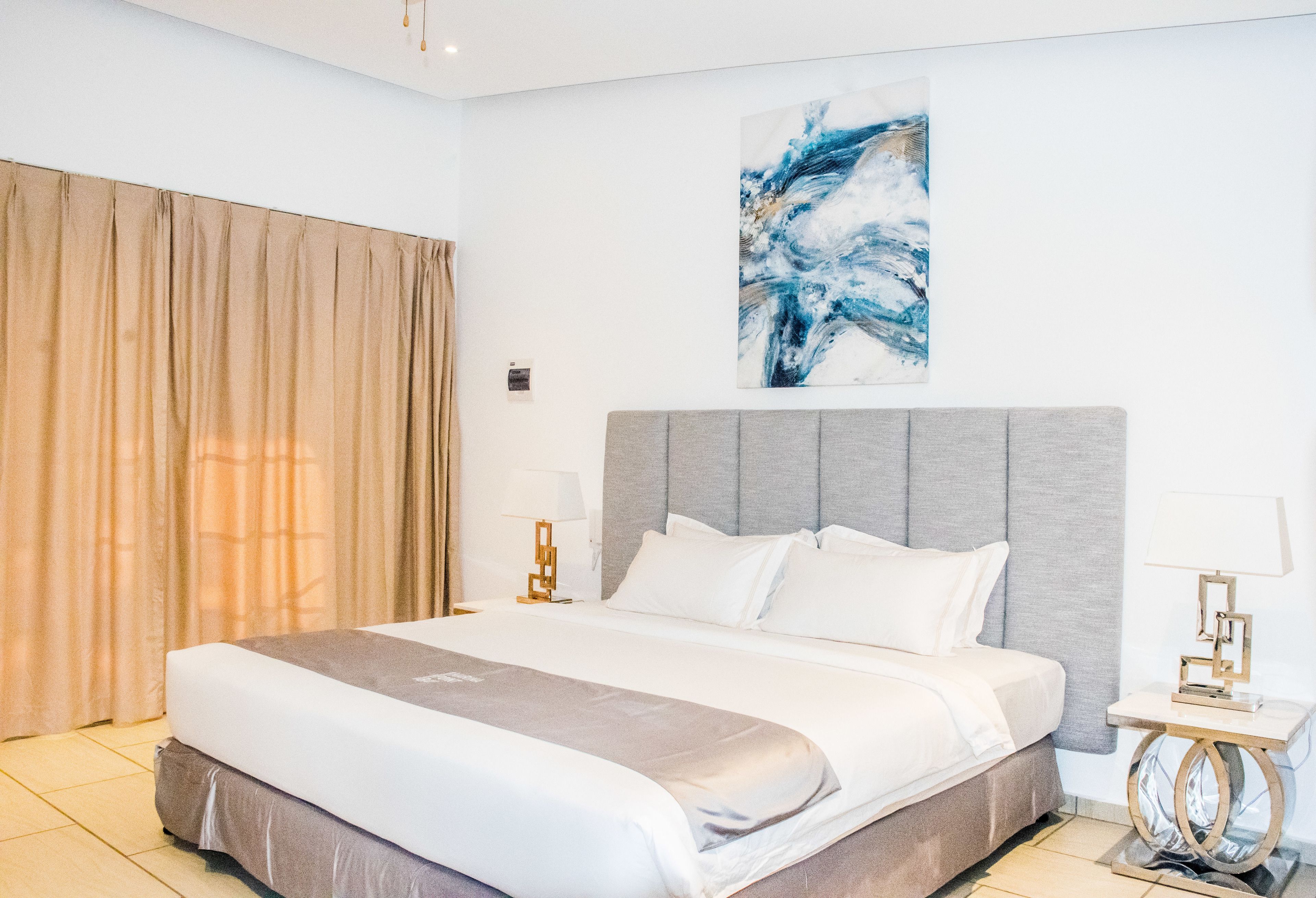 Une chambre d’hôtel moderne avec un grand lit, une tête de lit grise et un tableau accroché au mur.