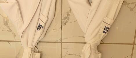 Two white robes tied to wall hooks in a bathroom with marble tiles.