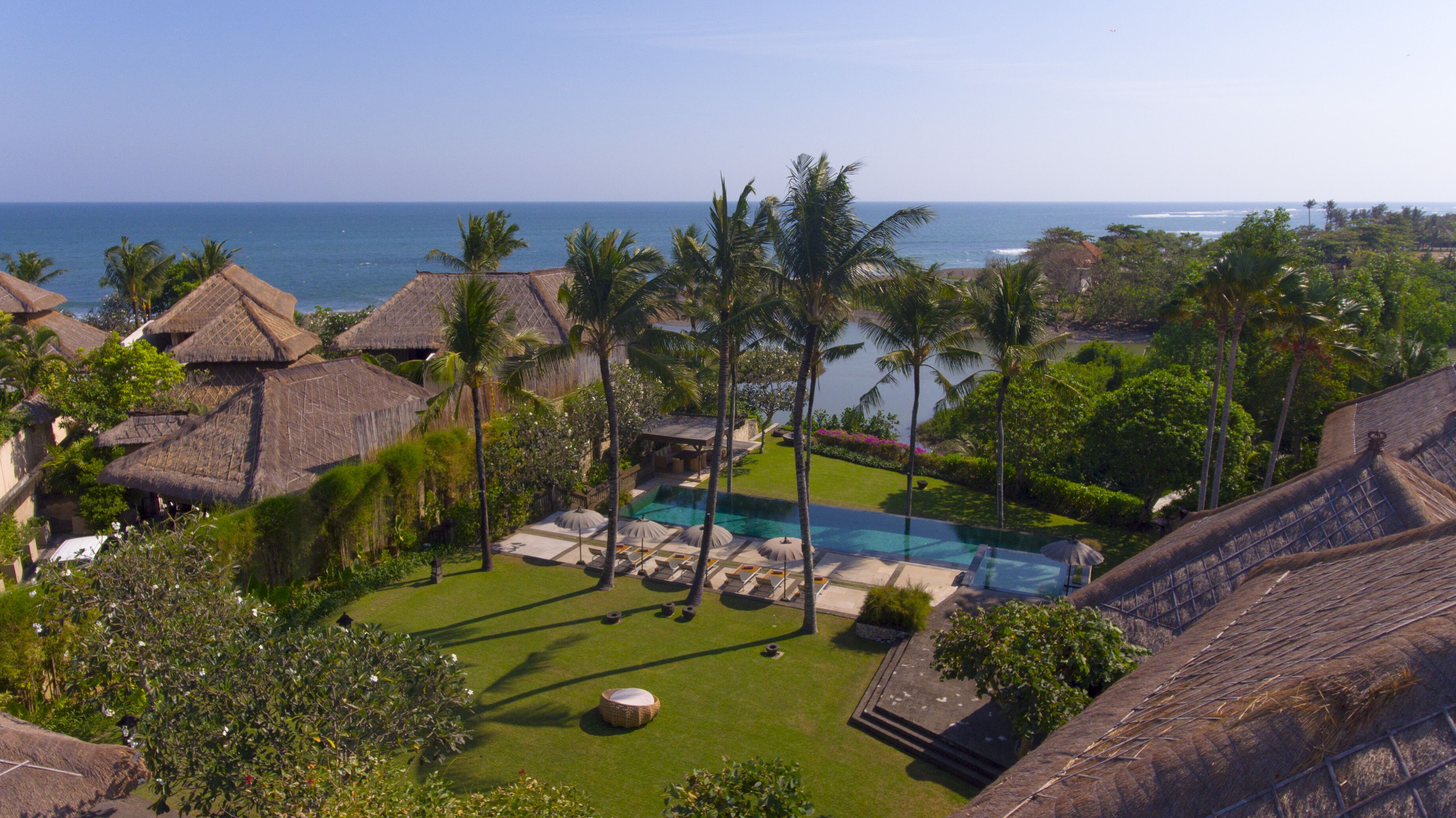 A resort with thatched-roof buildings, a swimming pool, and a view of the ocean.