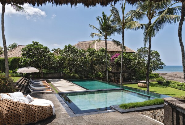 A pool area with lounge chairs, a thatched-roof structure, and a view of the beach.