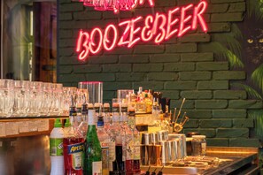 Zona de bar con un letrero de neón que dice 'BOOZE BEER' y varias botellas y vasos en estantes.