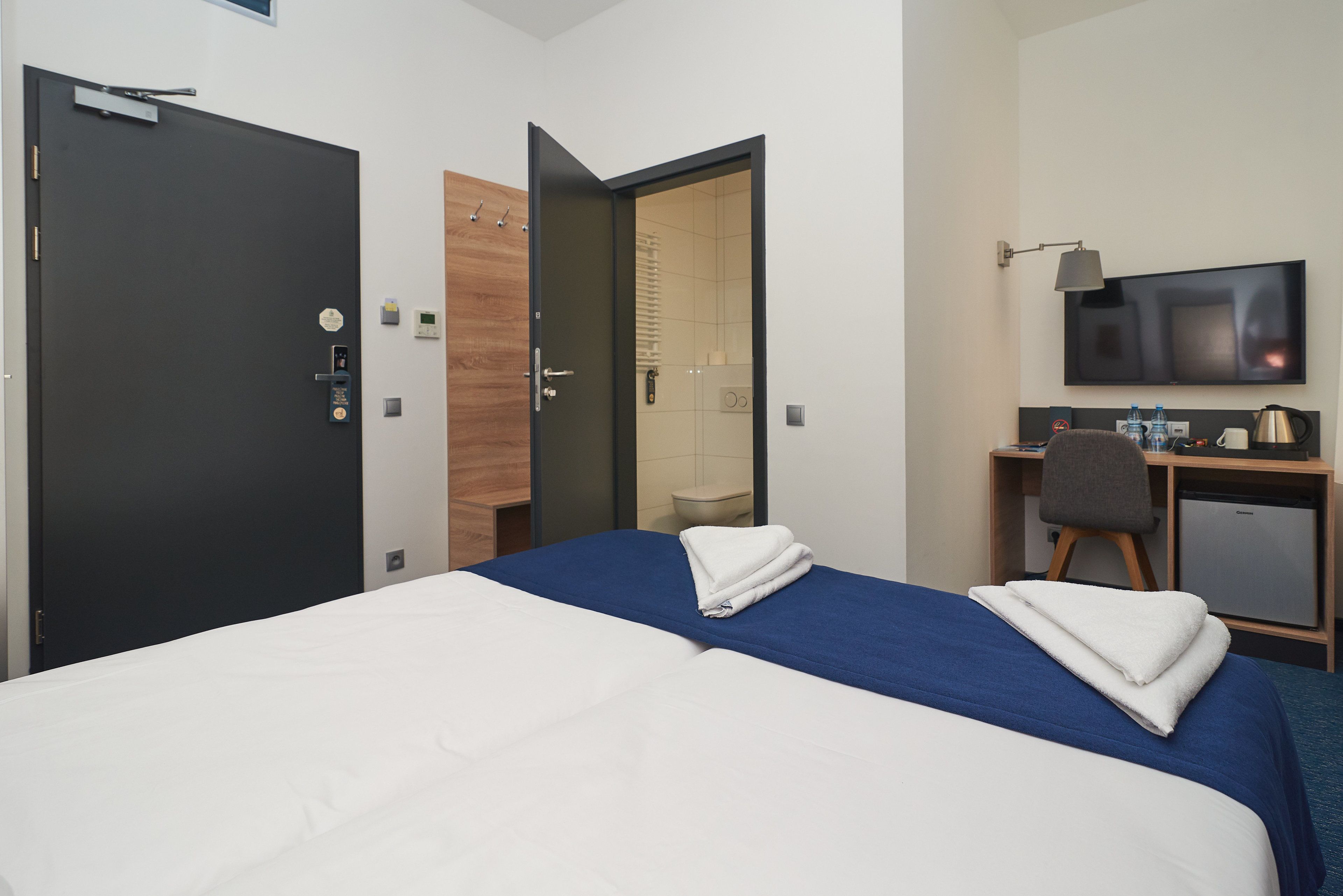 A hotel room with two beds, a desk with a chair, a television, and a small kitchenette.