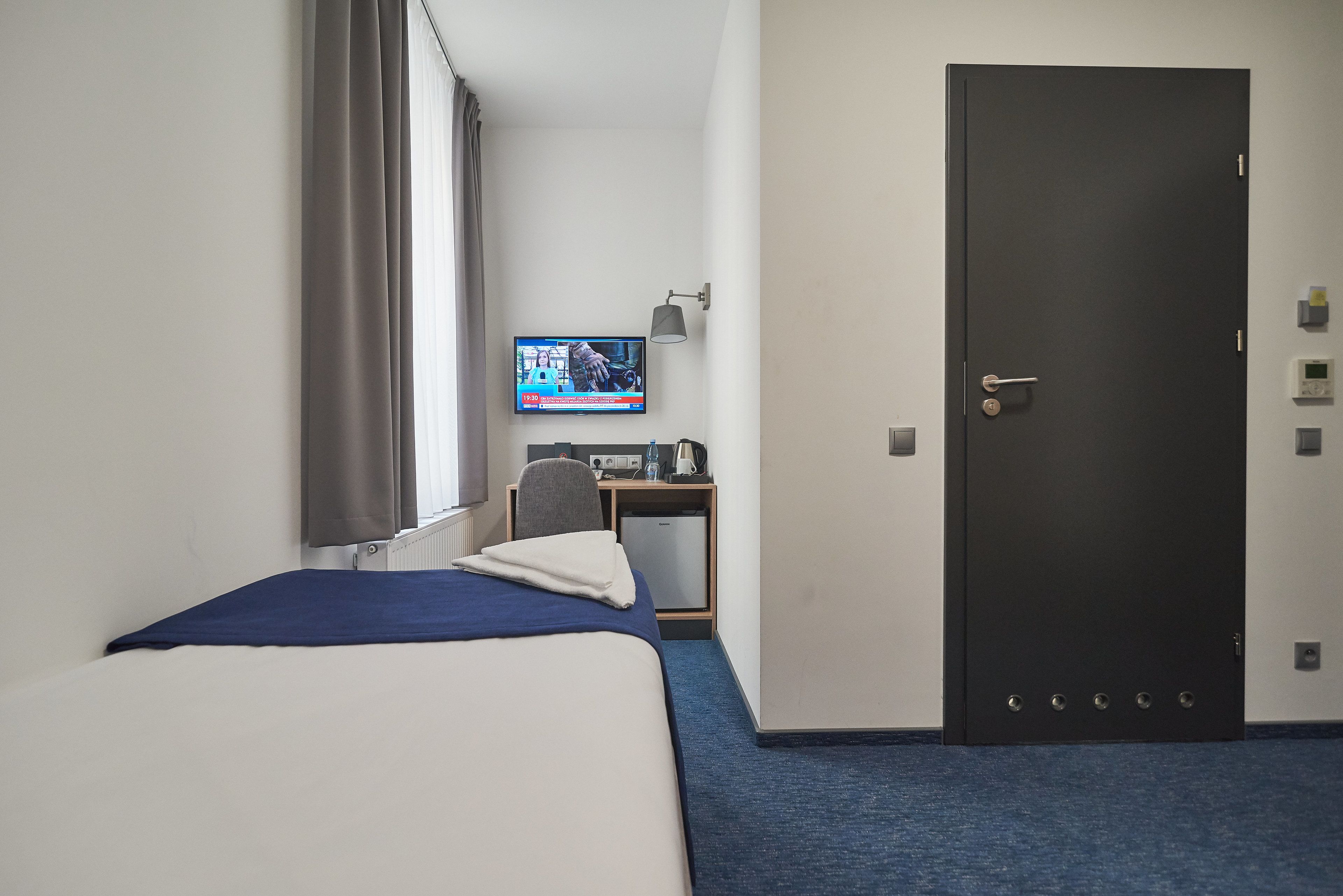 A hotel room with a bed, a desk, a television, and a door.