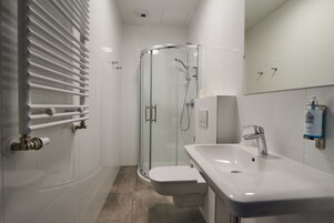 A modern bathroom with a glass-enclosed shower, a white sink, and a toilet.