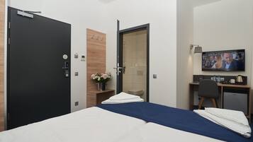 A hotel room with a bed, a desk with a chair, a television, and a door.