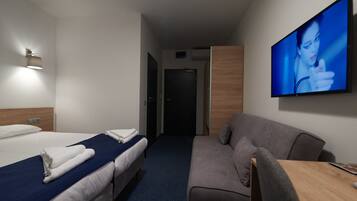 Habitación de hotel con dos camas, un sofá, un televisor y un armario de madera.