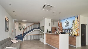 Uma área de recepção moderna com balcão de madeira, escada e sofá cinza.