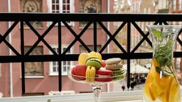 A table with lemons, limes, and a pitcher of lemonade, with a balcony railing and a building in the background.