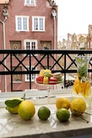 A table with lemons, limes, and a pitcher of lemonade, with a balcony railing and a building in the background.