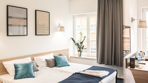 Quarto de hotel com uma cama grande, duas mesas de cabeceira, uma escrivaninha e uma janela com cortinas.