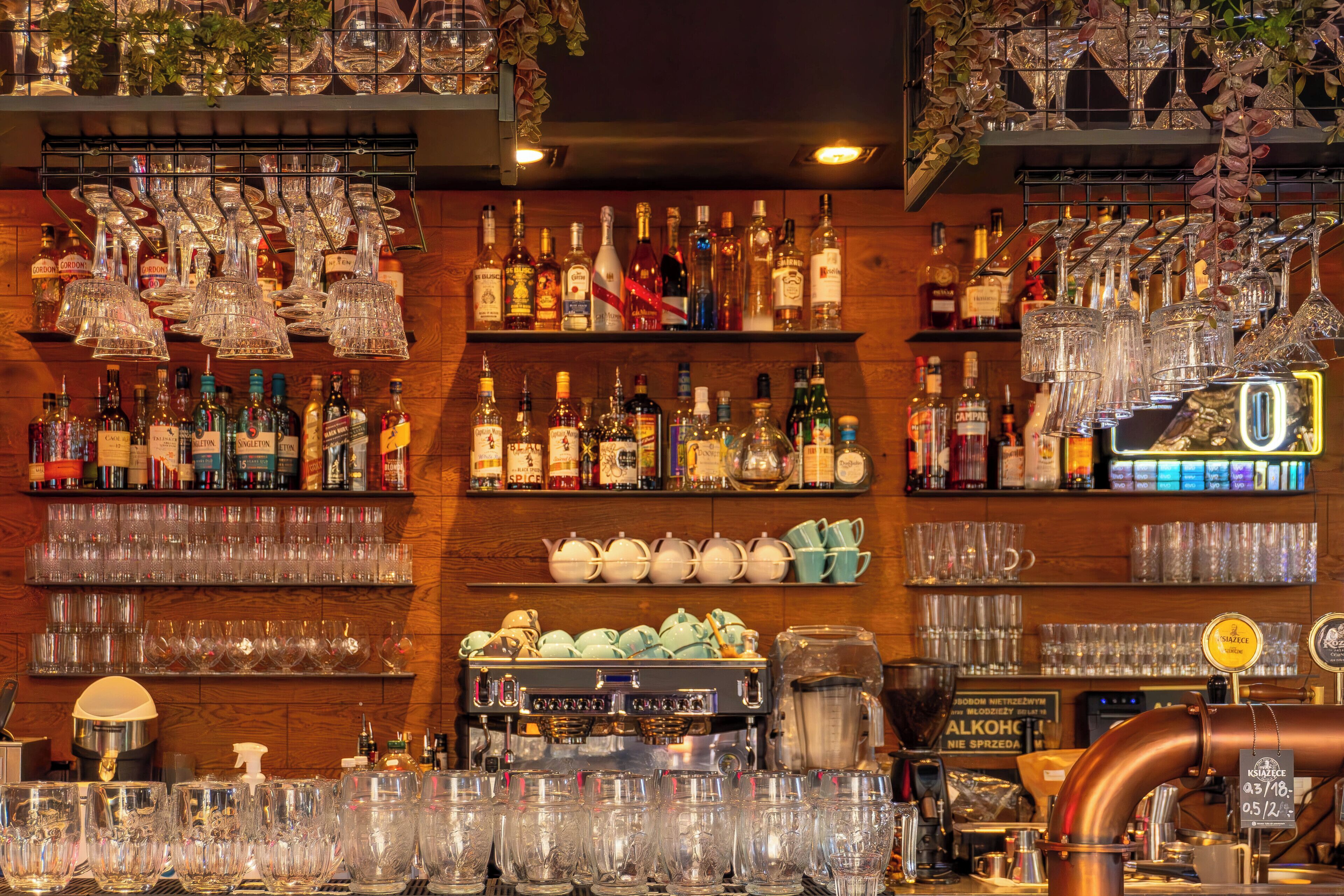 A bar area with shelves of liquor bottles, glasses, and a coffee machine.