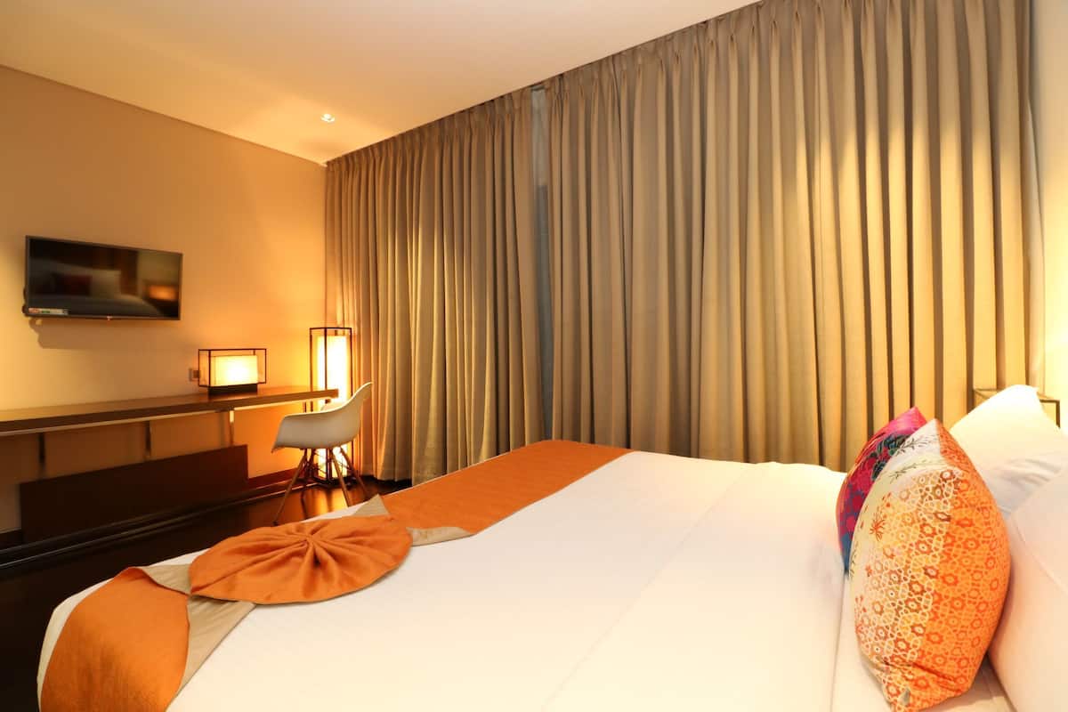 A hotel room with a large bed, a desk, a chair, and a television on the wall.