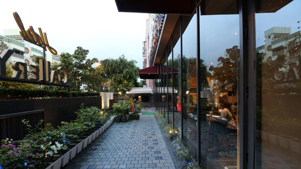 A pathway lined with potted plants and a glass building with a sign. - Hotel Gallery 67 (Kolkata)