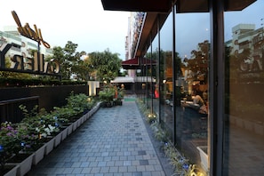 A pathway lined with potted plants and a glass building with a sign. - Hotel Gallery 67 (Kolkata)