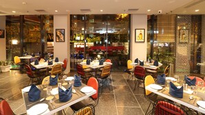 A restaurant with multiple tables and chairs, some with blue napkins. - Hotel Gallery 67 (Kolkata)