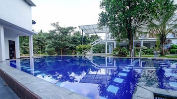 Una piscina con fondo de cristal, rodeada de vegetación y un edificio blanco.