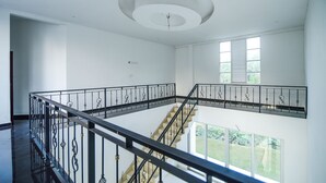 Ett rymligt interiört utrymme med en central trappa, vita väggar och utsikt över grönområden utanför.