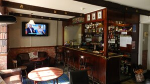 A bar area with a television mounted on the wall, wooden bar counter, stools, and a brick wall. - The Castle Hotel (Coldstream)