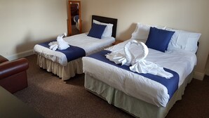 A hotel room with two beds, each with a blue bedspread and white linens. There are two white towels arranged on each bed. - The Castle Hotel (Coldstream)