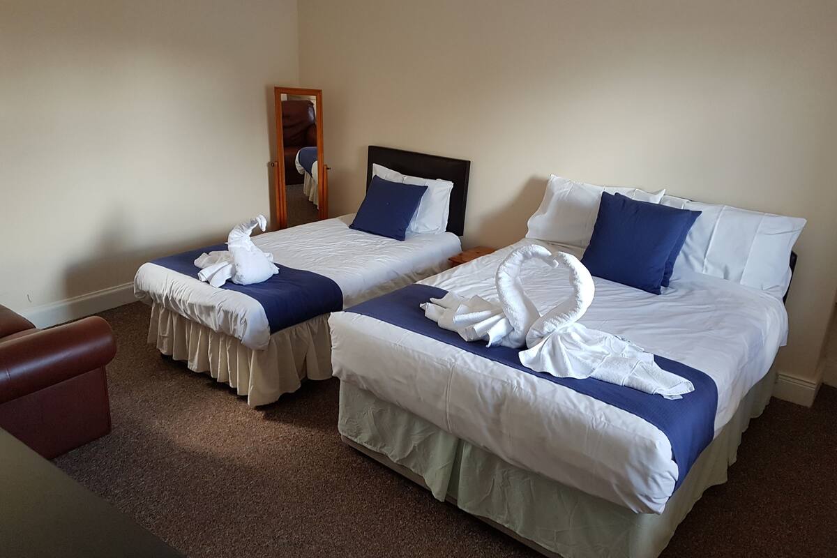 A hotel room with two beds, each with a blue bedspread and white linens. There are two white towels arranged on each bed.