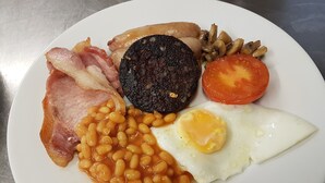 A plate with bacon, eggs, beans, mushrooms, sausages, and a tomato. - The Castle Hotel (Coldstream)