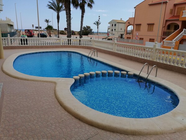 A swimming pool with a white fence and palm trees in the background.