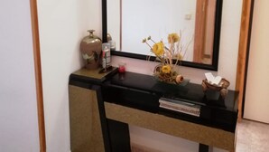 A black console table with a mirror above it, a small vase with yellow flowers, and a decorative plate on the wall. - Bitacora 4º Solo Familias! (Xeraco Playa)