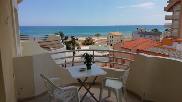 A balcony with a table and chairs, overlooking a beach and a clear sky. - Bitacora 4º Solo Familias! (Xeraco Playa)