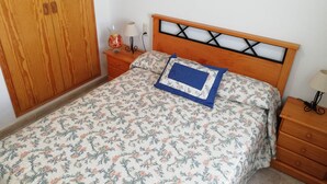 A bedroom with a wooden headboard, floral bedding, a bedside table with a lamp, and a wardrobe. - Bitacora 4º Solo Familias! (Xeraco Playa)