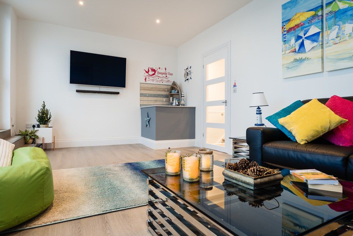 A modern living room with a flat-screen TV, a sofa, a coffee table with candles, and a painting on the wall.