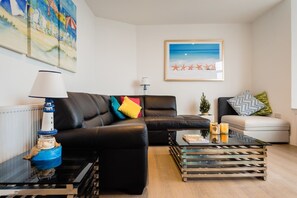A living room with a black leather sofa, a glass coffee table, and a framed picture of a beach scene.